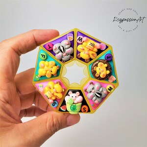 May include: A yellow octagonal shaped box with eight compartments, each featuring a different animal character made of colorful polymer clay. The box is decorated with letters, including "T", "I", "S", and "M".
