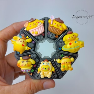 May include: A seven-day pill organiser with a cute cartoon character on each day of the week. The characters are yellow with brown accents and are wearing different outfits. The pill organiser is black with white lettering.