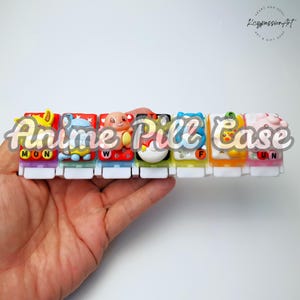 Op de afbeelding: Een veelkleurige pillendoos met anime-personages op elk compartiment. De doos is gelabeld met de dagen van de week: MON, TUE, WED, THU, FRI, SAT, SUN.