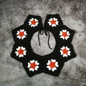May include: Black crochet collar with white and orange flower accents.