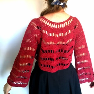 Puede incluir: Top de crochet rojo con un ajuste holgado y mangas largas. La parte superior tiene un delicado patr&oacute;n de calado y una longitud recortada.