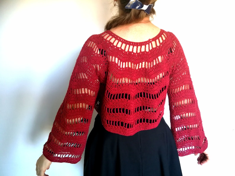 Puede incluir: Top de crochet rojo con un ajuste holgado y mangas largas. La parte superior tiene un delicado patr&oacute;n de calado y una longitud recortada.