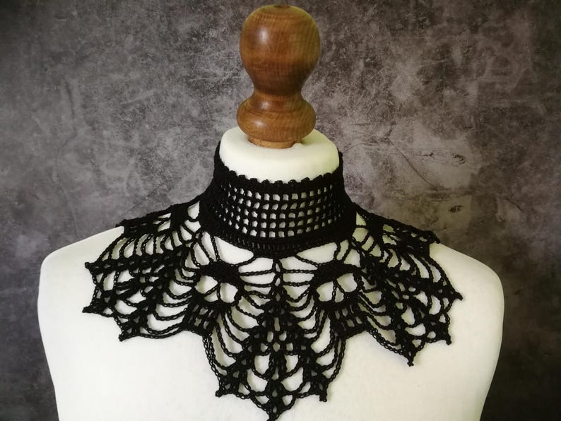 Puede incluir: Cuello de ganchillo negro con dise&ntilde;o de telara&ntilde;a. El cuello se muestra en un busto de maniqu&iacute; blanco con cuello de madera. El cuello tiene un escote tipo gargantilla y un patr&oacute;n calado detallado.