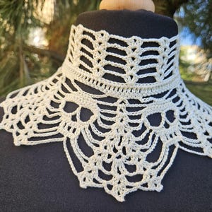 Puede incluir: Un collar blanco de ganchillo con un diseño delicado y de encaje. El collar está hecho con un hilo fino y tiene un borde festoneado.