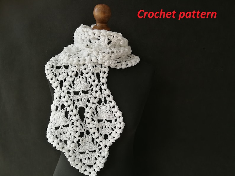 May include: White crochet scarf with a delicate, lacy pattern. The scarf is draped over a black mannequin.