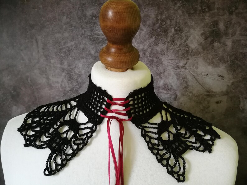 Puede incluir: Cuello de ganchillo negro con cierre de lazo de cinta roja. El cuello se muestra en un busto de maniqu&iacute; blanco. El dise&ntilde;o de encaje y la cinta roja a&ntilde;aden un toque de elegancia a este accesorio &uacute;nico.