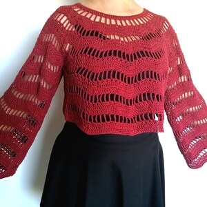 Puede incluir: Un top de crochet rojo con mangas largas y un patr&oacute;n ondulado. El top es corto y tiene un escote redondo.