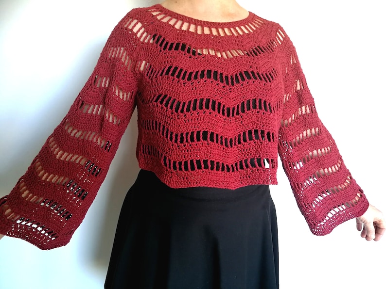 Puede incluir: Un top de crochet rojo con mangas largas y un patr&oacute;n ondulado. El top es corto y tiene un escote redondo.