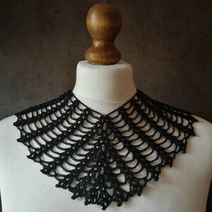 May include: A black crocheted collar with a delicate, lacy design. The collar is displayed on a white mannequin.