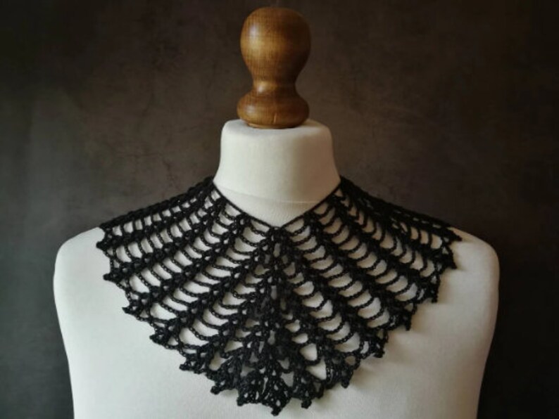 May include: A black crocheted collar with a delicate, lacy design. The collar is displayed on a white mannequin.
