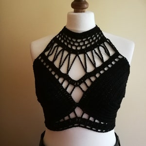 May include: A black crochet halter top displayed on a mannequin. The top features a high neckline and a geometric design across the chest. The crochet work is intricate, with open spaces creating a textured look. The top is a solid black color.