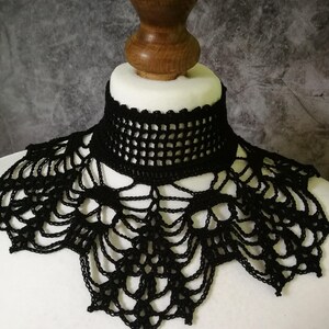 Puede incluir: Un collar negro de ganchillo con un dise&ntilde;o similar a una telara&ntilde;a. El collar tiene un escote alto y estructurado y un borde festoneado. El intrincado encaje se muestra sobre una cabeza de maniqu&iacute; blanca sobre un fondo gris.