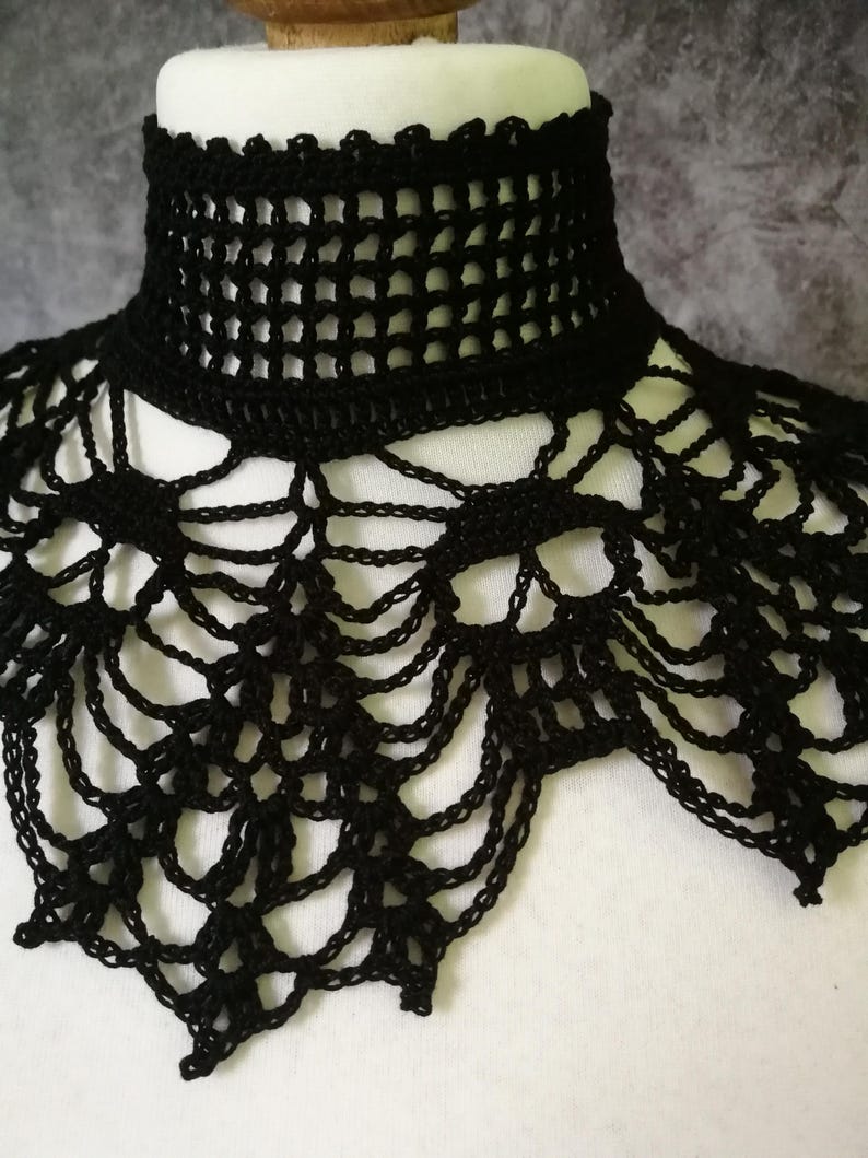 Puede incluir: Un cuello de ganchillo negro con un cuello alto y estructurado y un dise&ntilde;o calado. El cuello se muestra en una cabeza de maniqu&iacute; blanca, destacando sus intrincados detalles y textura. El dise&ntilde;o del cuello presenta una combinaci&oacute;n de patrones geom&eacute;tricos y fluidos.