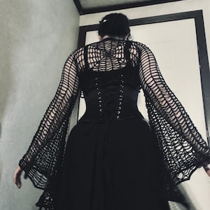 May include: A black mesh top with long sleeves and a spiderweb pattern. The top is worn over a black corset with a lace-up back.