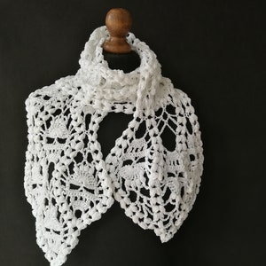 May include: White crocheted lace scarf with a delicate floral pattern. The scarf is displayed on a wooden mannequin.