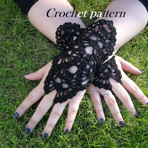 May include: A pair of black crochet fingerless gloves with a lacy design. The gloves are lying on a bed of green grass. Crochet pattern.