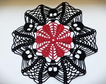May include: A black and red crocheted doily with a skull design. The center of the doily is a red crocheted flower.