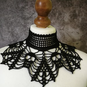 Puede incluir: Collar negro de ganchillo, exhibido en un busto de maniqu&iacute; blanco. El collar presenta un dise&ntilde;o detallado de tejido abierto alrededor del cuello y un patr&oacute;n decorativo de encaje que se extiende por el pecho. El fondo es gris moteado.