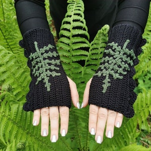 May include: A pair of black fingerless gloves with green fern leaf designs. The gloves are crocheted and have a scalloped edge.
