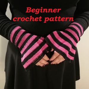 Puede incluir: Un par de calentadores de brazo de crochet a rayas negras y rosas. Los calentadores de brazo se muestran en una persona que lleva una camisa negra de manga larga y una falda negra. El texto "Beginner crochet pattern" está escrito en rojo en la imagen.
