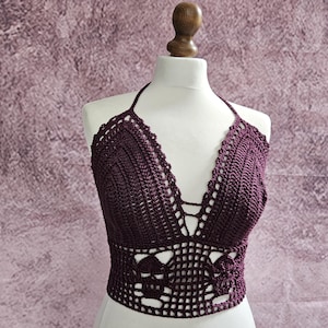 May include: A burgundy crochet halter top with a deep V-neckline and intricate detailing. The top is made with a delicate crochet stitch and has a cropped length.