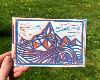 May include: A linocut print of a mountain range with a blue and orange color scheme. The mountain peaks are geometric and the foreground is a stylized wave.