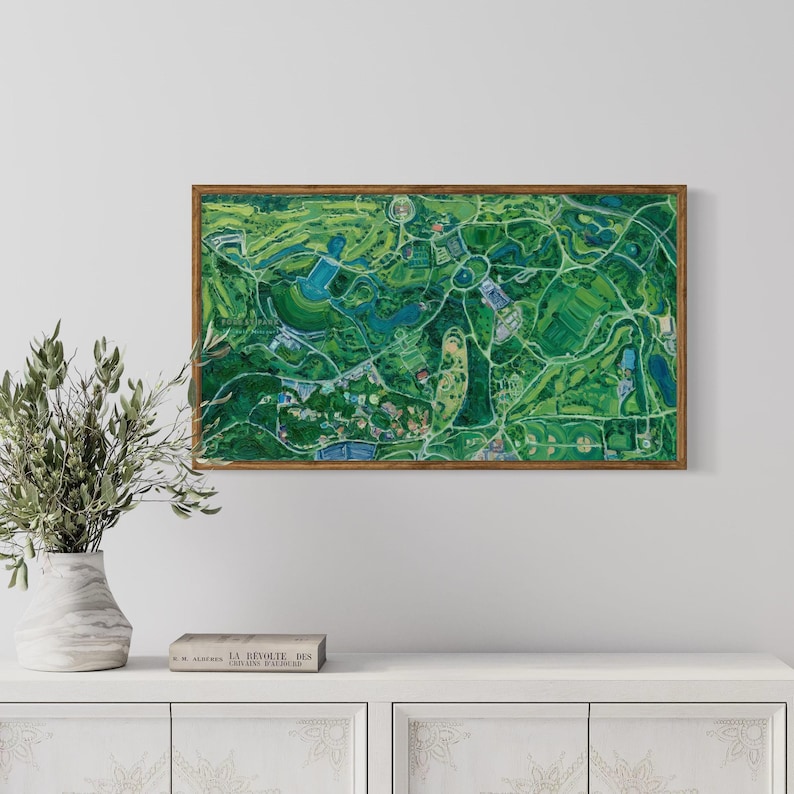 The vibrantly green and colorful Forest Park painting framed in oak on white wall in home interior setting above a simple wooden console with a book and a vase with greenery.