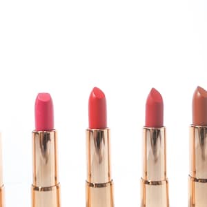 May include: Five lipstick tubes with gold caps and different shades of lipstick: nude, pink, red, coral, and brown.