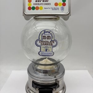 May include: Vintage silver M&M's candy dispenser with a glass globe and a sign that reads "m&ms CHOCOLATE CANDIES".