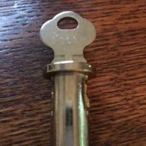 May include: A silver key with a round head and a long, cylindrical shaft. The key has the word "TO" engraved on the head.