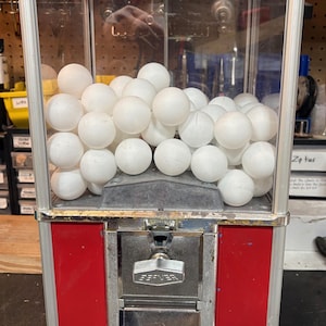 May include: Vintage gumball machine with a clear glass display filled with white gumballs. The machine has a red and silver metal frame, with the brand name "Effenver" visible on the front.