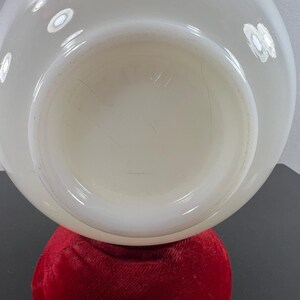May include: A white milk glass bowl with a smooth, rounded surface. The bowl is sitting on a red velvet cushion.
