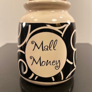 May include: White ceramic jar with a black and white swirl design. The jar has a cork lid and says "Mall Money" in black lettering.