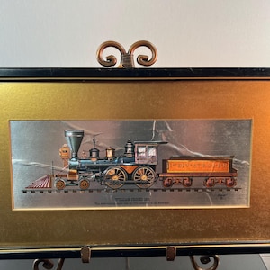 May include: Framed print of a vintage train, featuring a black and gold frame with a gold and silver background. The train is detailed with black, blue, orange, and gold accents. The text "WILLIAM CROOKS 1861" is visible below the train.