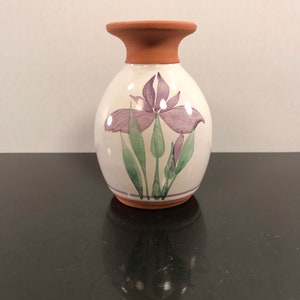 May include: A white ceramic vase with a terracotta rim, featuring a hand-painted purple iris flower design with green leaves.