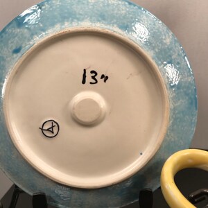 May include: A blue and white ceramic plate with a white center and a blue rim. The plate has a handwritten inscription "13" on the back.
