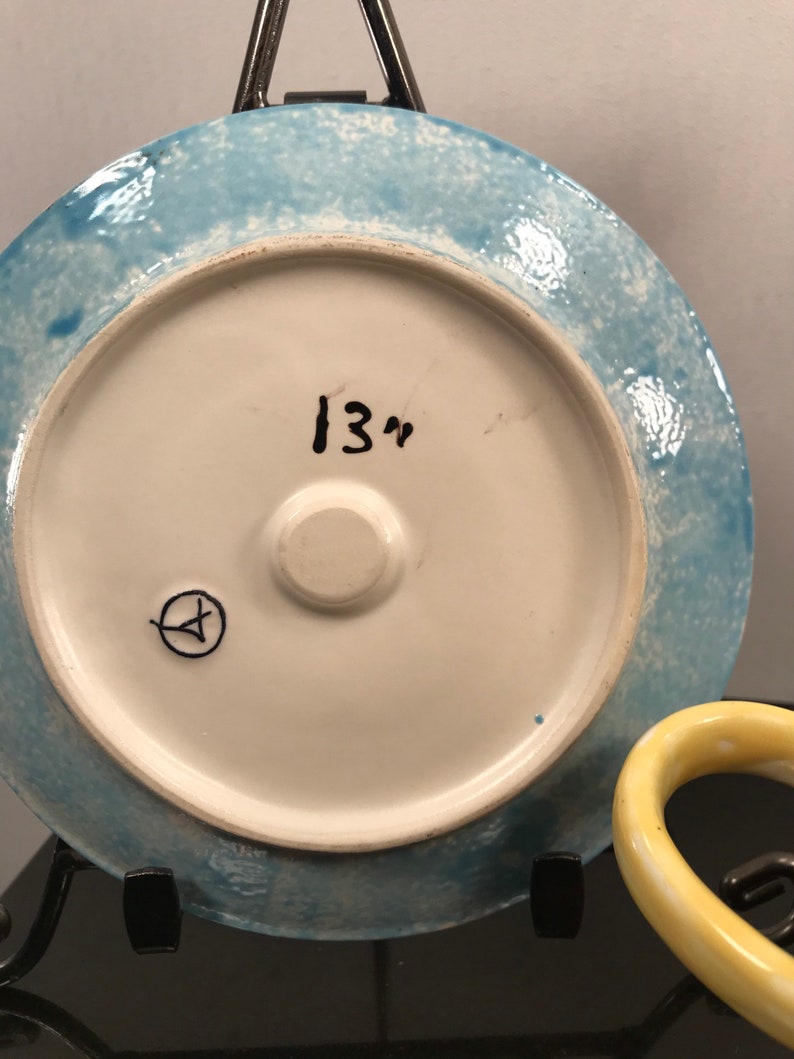 May include: A blue and white ceramic plate with a white center and a blue rim. The plate has a handwritten inscription "13" on the back.