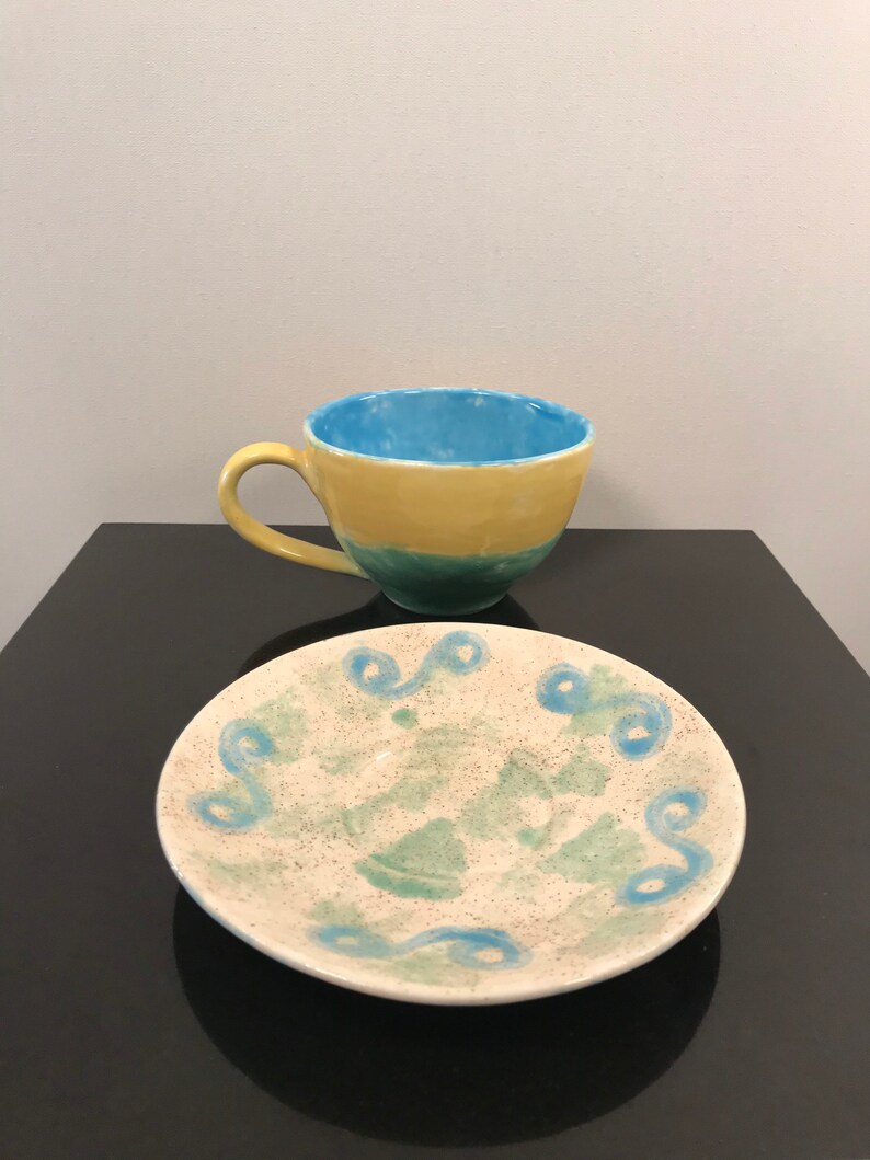 May include: A yellow, green, and blue ceramic teacup and saucer set with a swirling blue design on the saucer.