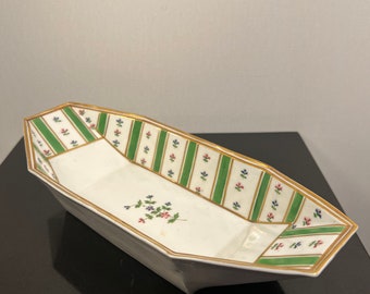 May include: White, octagonal serving dish with a gold rim. The dish features green and white striped accents with floral details. A small floral arrangement is in the center of the dish.