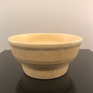 May include: A pale yellow ceramic bowl with a fluted design. The bowl is empty and sitting on a black surface.