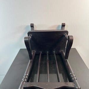 May include: A dark brown wooden chair with a rectangular seat and four vertical back supports. The chair's legs are slightly curved and have decorative detailing. The chair is positioned upside down, showcasing its underside.