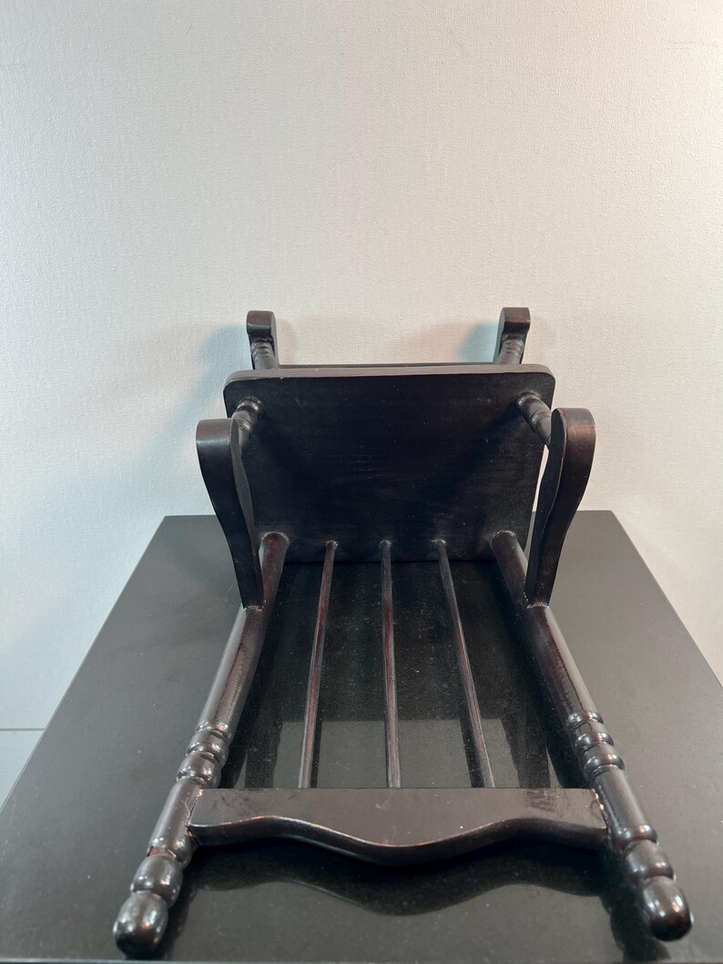 May include: A dark brown wooden chair with a rectangular seat and four vertical back supports. The chair's legs are slightly curved and have decorative detailing. The chair is positioned upside down, showcasing its underside.