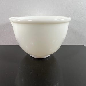 May include: A white ceramic mixing bowl with a pouring spout. The bowl is on a black surface.