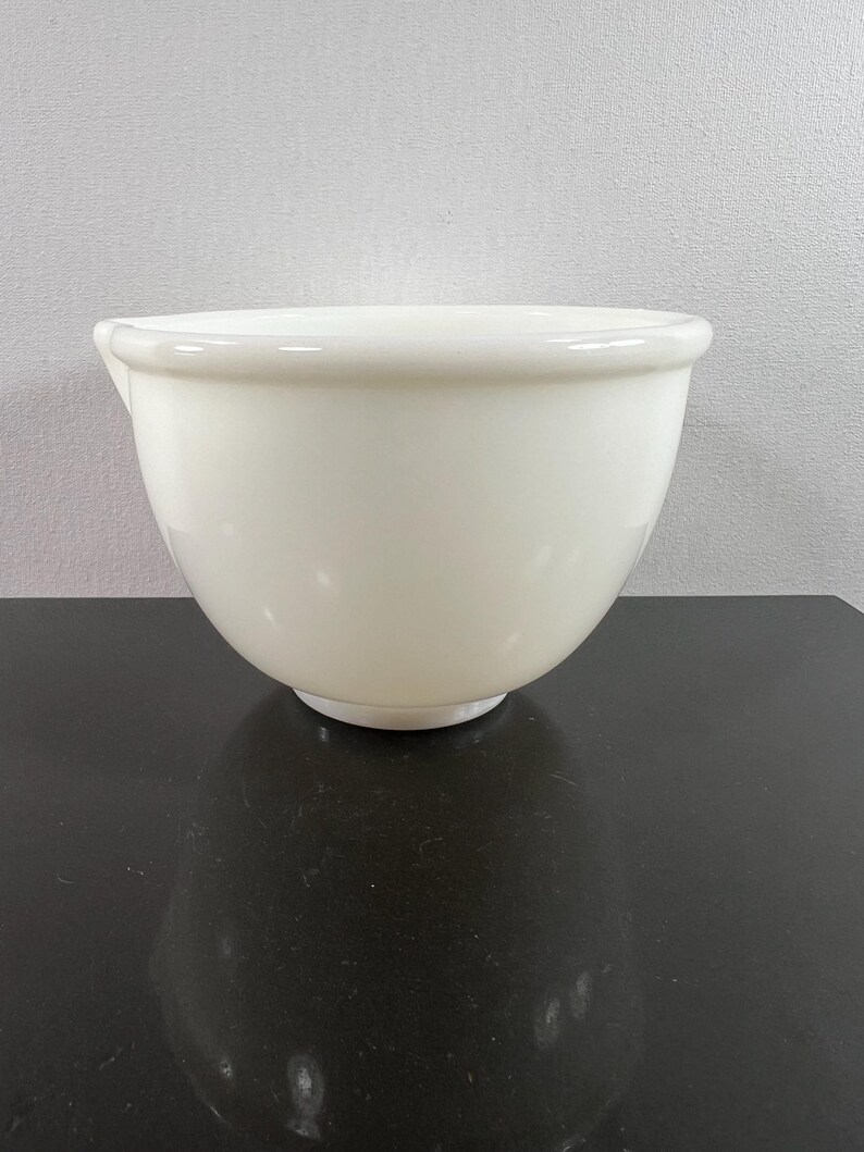May include: A white ceramic mixing bowl with a pouring spout. The bowl is on a black surface.