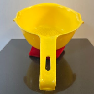 May include: A yellow plastic colander with a handle. The colander has a strainer at the bottom.