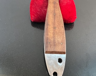 May include: A fish-shaped bottle opener with a wooden handle and a stainless steel opener. The opener is resting on a red velvet surface. The handle has a dark brown finish.