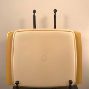 May include: A gold and white plastic serving tray with a black metal stand. The tray has a circular design in the center.