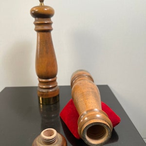 Peut inclure: Deux moulins &agrave; sel et &agrave; poivre en bois avec une base en laiton. Les moulins sont de couleur marron et ont une forme cylindrique. Un moulin est couch&eacute; sur le c&ocirc;t&eacute; sur un coussin en velours rouge. L'autre moulin est debout sur une surface noire.