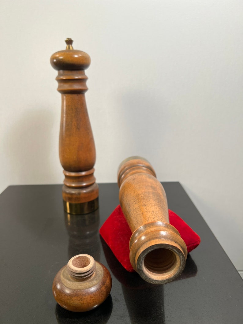 Peut inclure: Deux moulins &agrave; sel et &agrave; poivre en bois avec une base en laiton. Les moulins sont de couleur marron et ont une forme cylindrique. Un moulin est couch&eacute; sur le c&ocirc;t&eacute; sur un coussin en velours rouge. L'autre moulin est debout sur une surface noire.