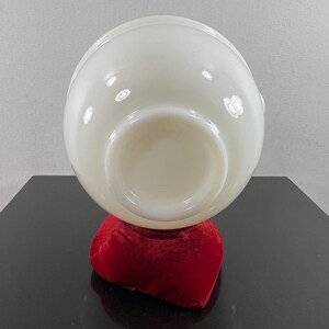May include: A white milk glass bowl with a rounded shape, sitting on a red velvet cushion. The bowl is empty and the bottom is visible.